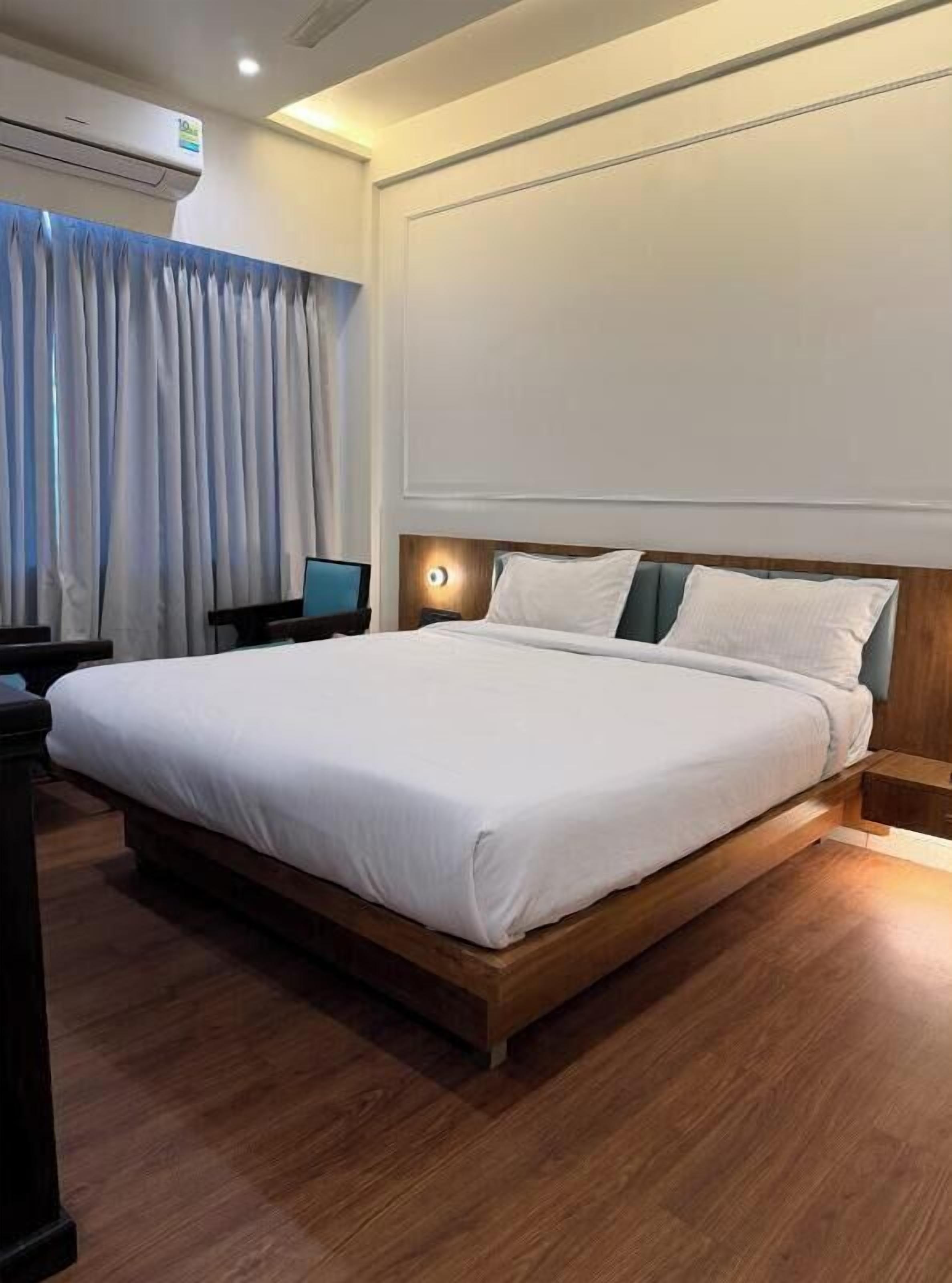 A hotel room with a large bed, a desk, and an air conditioning unit.