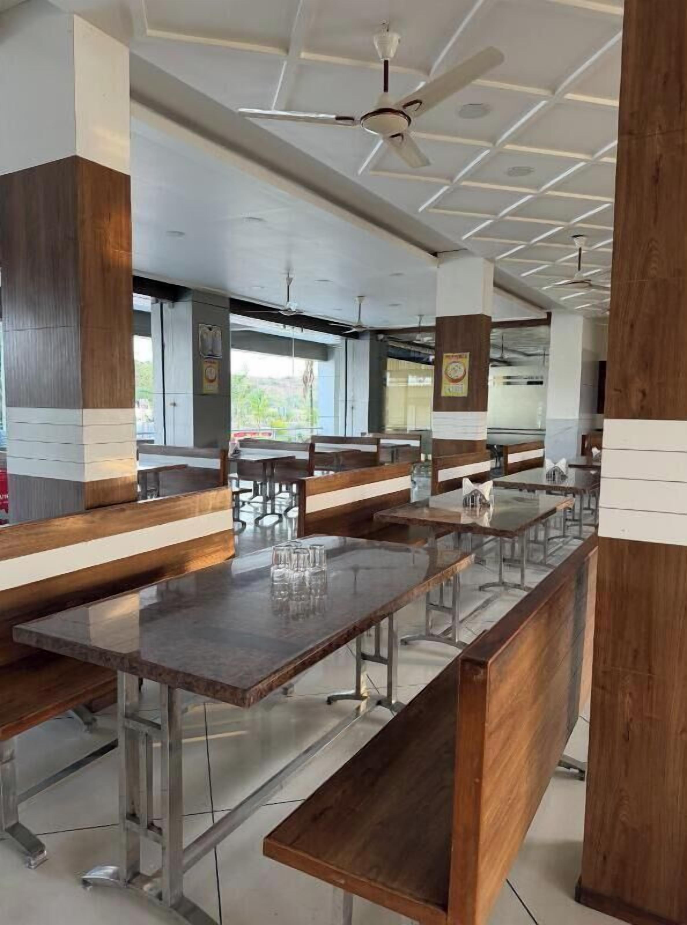 Una cafetería moderna con mesas compartidas largas, bancos e ventiladores de techo.
