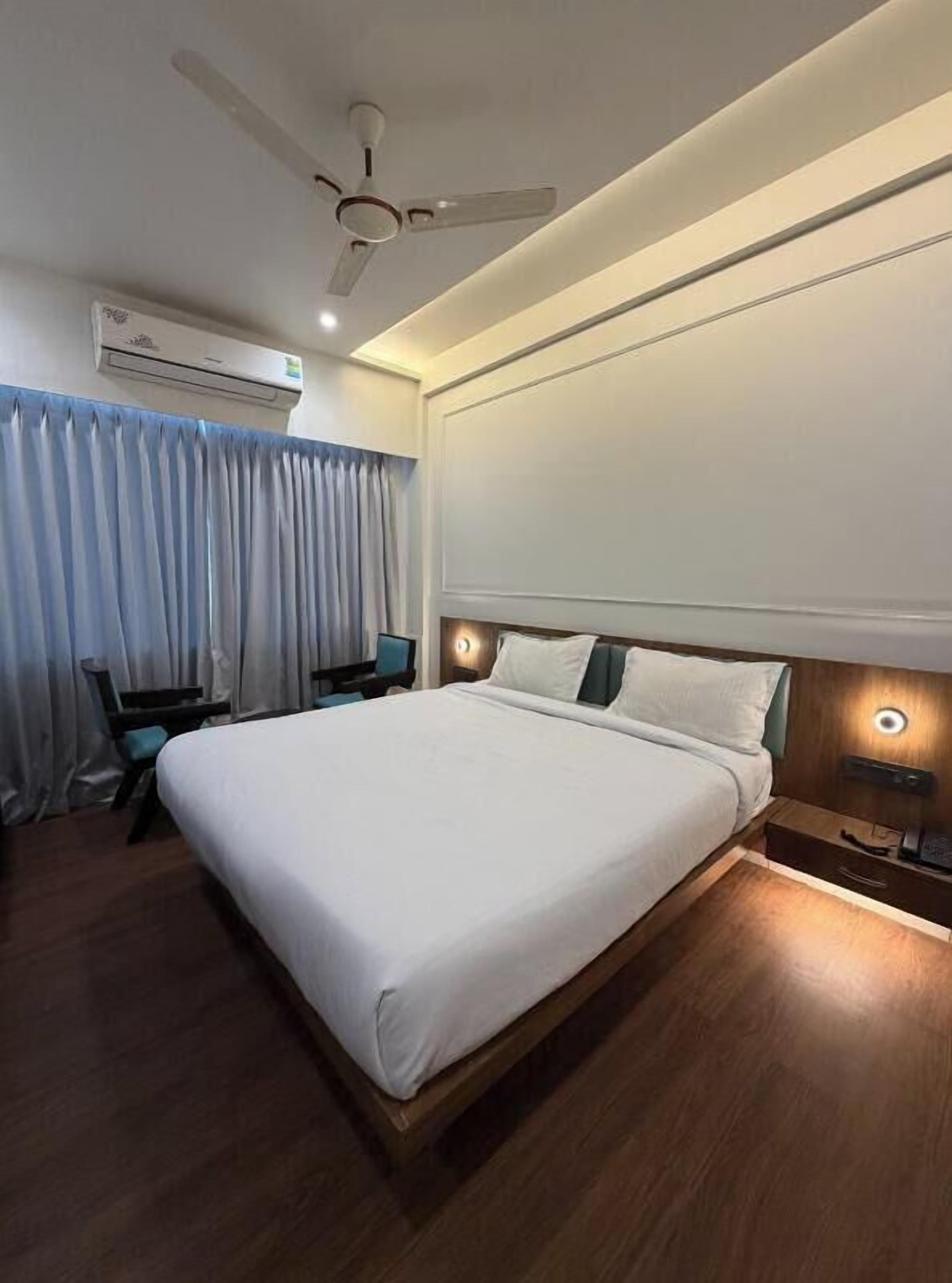 A hotel room with a bed, a desk, a chair, an air conditioning unit, and a ceiling fan.