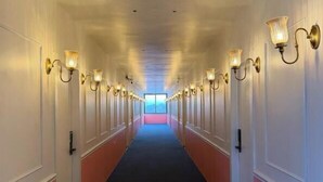 Un couloir d’hôtel avec un sol recouvert de moquette, des murs blancs et des luminaires fixés au mur.