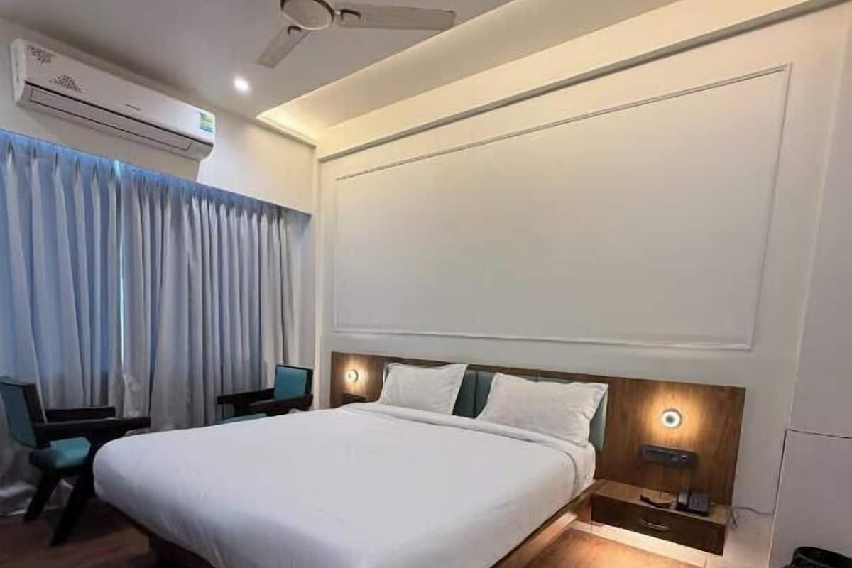 Una camera d'hotel moderna con un letto grande, una ventola a soffitto, un condizionatore d'aria, una scrivania con sedia e un comodino con lampada.