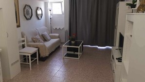 Una sala de estar con un sofá, una mesita, un televisor y una ventana con cortinas.
