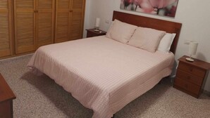 Un dormitorio con cama, mesitas de noche, un armario de madera y una obra de arte en la pared.