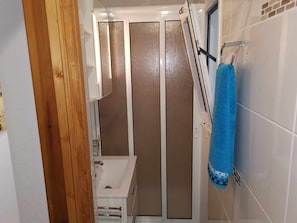 Casa de banho com uma pia branca, cabine de duche em vidro e uma toalha azul num suporte.
