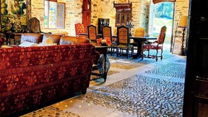 A cozy room with a patterned sofa, a dining table with chairs, a stone floor, and a large window. - Chateau for rent (Aix)