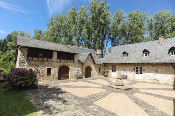 A stone building with a courtyard, wooden doors, and a small garden with flowers. - Chateau for rent (Aix)