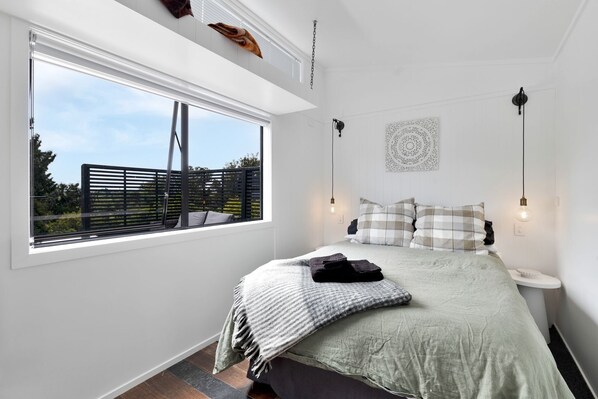 Ein Schlafzimmer mit großem Fenster, einem Bett mit grüner Bettdecke, zwei Nachttischlampen und einem Wanddekor.