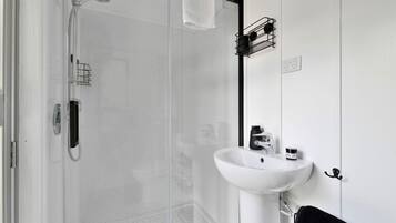 Een moderne badkamer met een douchecabine van glas, een witte wastafel en een zwarte handdoekhouder.