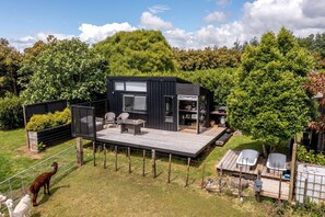 A modern outdoor living space with a deck, seating area, and a small building with windows and a door. - Charming Tiny House Surrounded by Trees in New Plymouth, North Island (new plymouth)