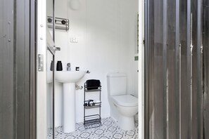 A small, white bathroom with a pedestal sink, toilet, and a metal rack for towels.