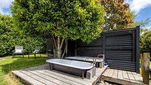 Eine Holzterrasse mit zwei Whirlpools, einem Baum und einer schwarzen Garagentür.