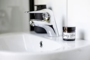 Un lavabo de salle de bain avec un robinet chromé et un pot de lotion pour le corps étiqueté « Lotion pour le corps » posé sur le comptoir.