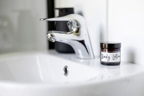 Un lavamanos con grifo cromado y un tarro de loción corporal etiquetado 'Body Lotion' sobre el mostrador.