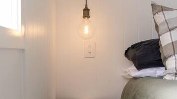 A small, white, round bathroom with a pedestal sink, a bedside table, and a hanging light fixture.