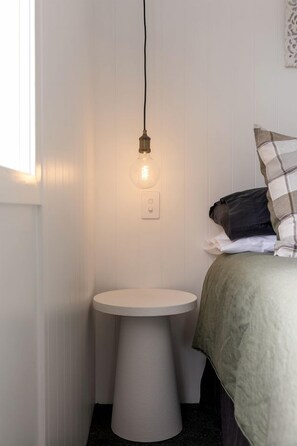 A small, white, round bathroom with a pedestal sink, a bedside table, and a hanging light fixture.