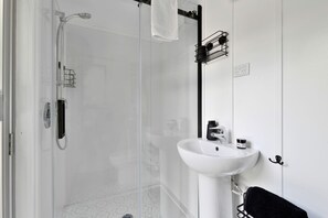 Un baño moderno con cabina de ducha de vidrio, un lavabo blanco y un toallero negro.