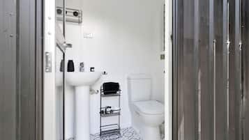 A small, white bathroom with a pedestal sink, toilet, and a metal rack for towels.