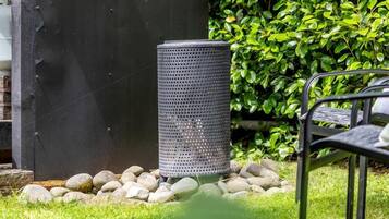 A garden area with a metal chair, a black trash bin, and a green hedge in the background.