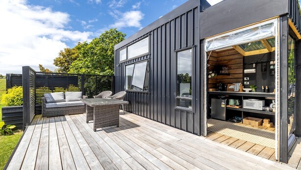 Eine moderne Terrassenanlage im Freien mit einer Couch und einem Tisch, einem Küchenbereich mit Schränken und Geräten sowie einem großen Fenster.