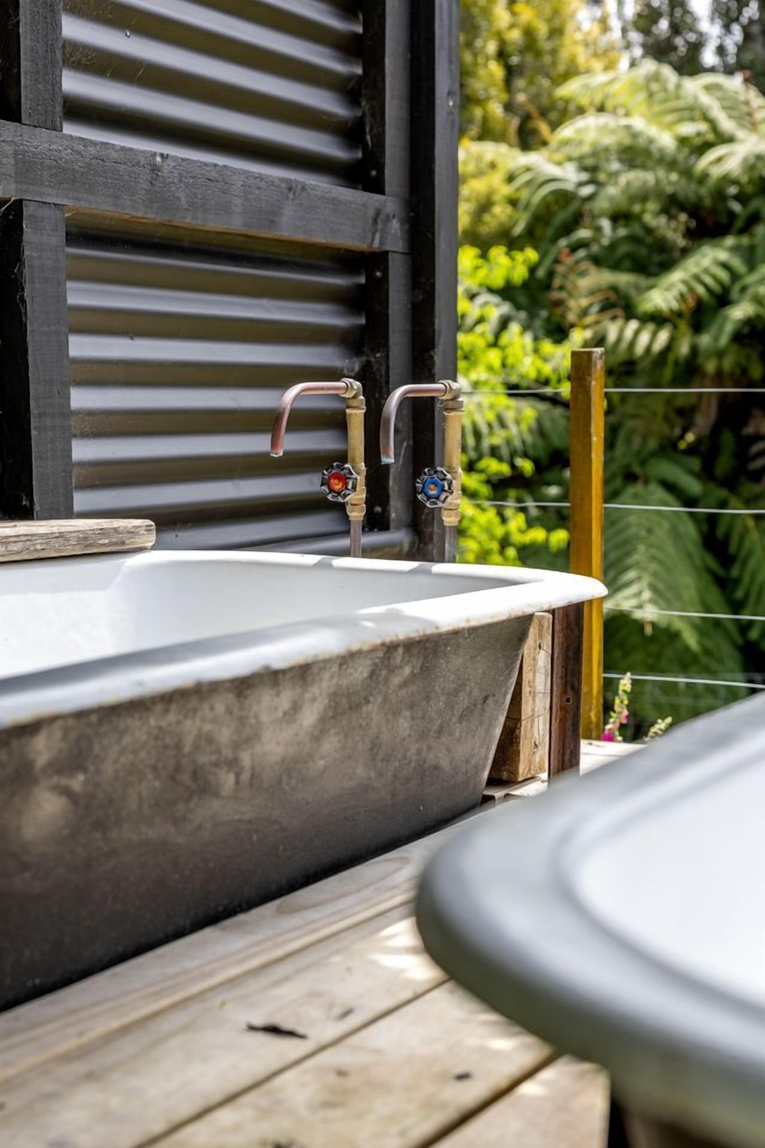 A bathtub with a wooden ledge, a faucet with a decorative handle, and a wooden railing.