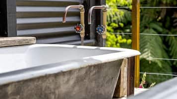 A bathtub with a wooden ledge, a faucet with a decorative handle, and a wooden railing.