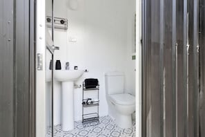 A small, white bathroom with a pedestal sink, toilet, and a metal rack for towels.