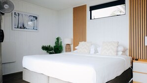 Ein Schlafzimmer mit einem Bett, einem Wandventilator, einer Pflanze und einem Fenster mit Jalousien.