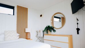 Une chambre à coucher avec un lit, une table de chevet, une lampe, un miroir, une télévision et une plante.
