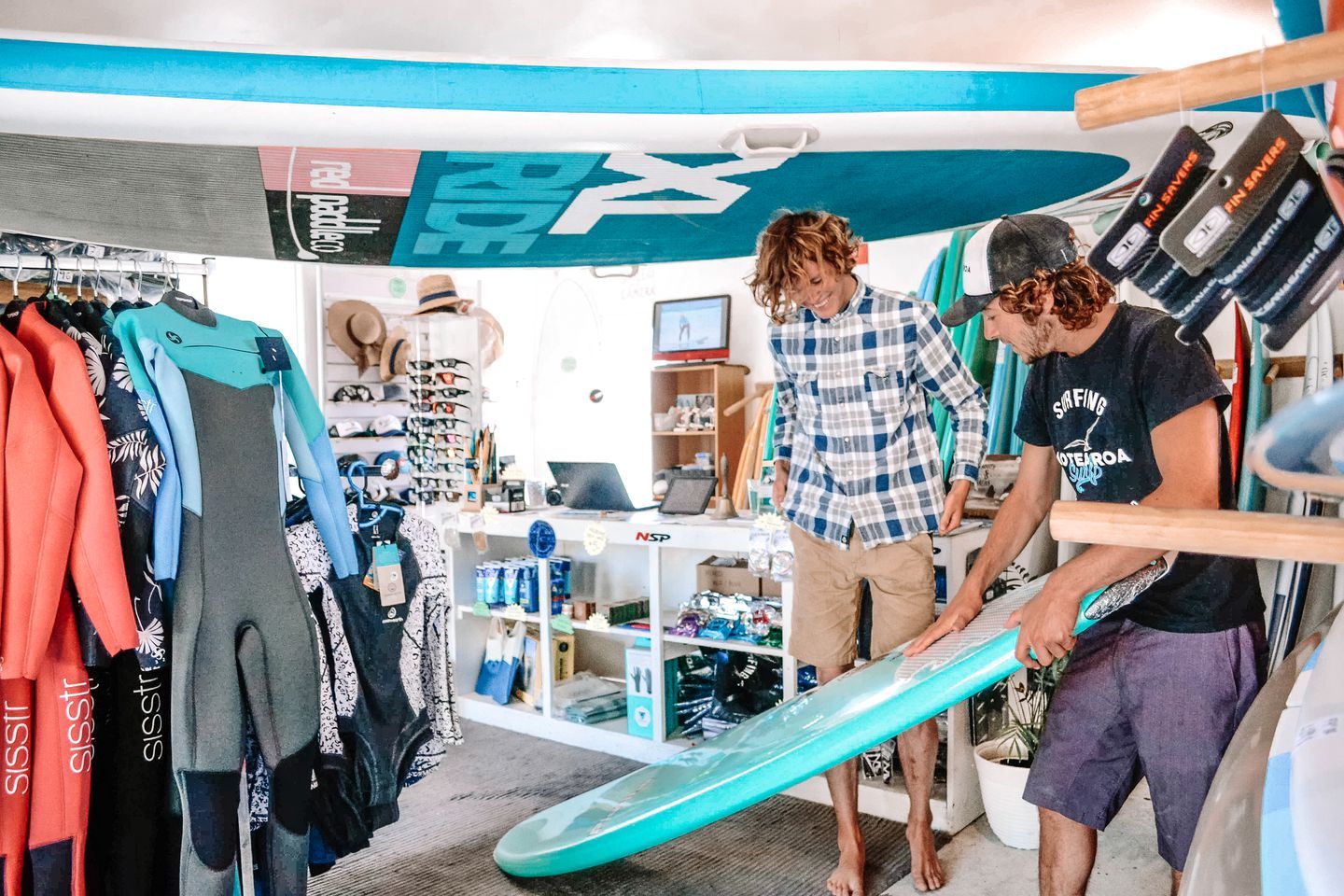 A surf shop with wetsuits, surfboards, and a laptop on a table.