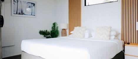 A bedroom with a bed, a wall-mounted fan, a plant, and a window with blinds.