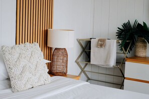 A neatly arranged bedroom with a bed, a lamp, a towel rack, and a plant.