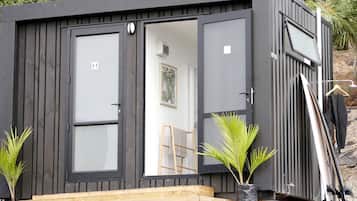 A compact, dark-colored cabin with a sliding door, a small porch, and a ladder.