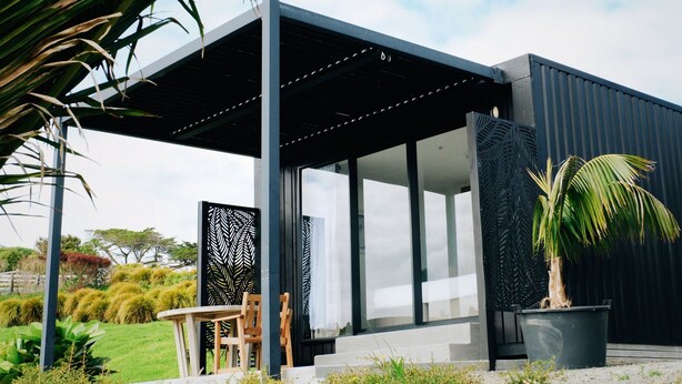 Un bâtiment moderne doté d’un patio couvert, de grandes fenêtres et d’un paravent décoratif.