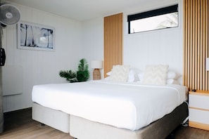 Ein Schlafzimmer mit einem Bett, einem Wandventilator, einer Pflanze und einem Fenster mit Jalousien.