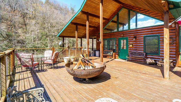 Eine Holzterrasse mit Feuerstelle, Sitzgelegenheiten im Freien und einer Hütte mit großen Fenstern.