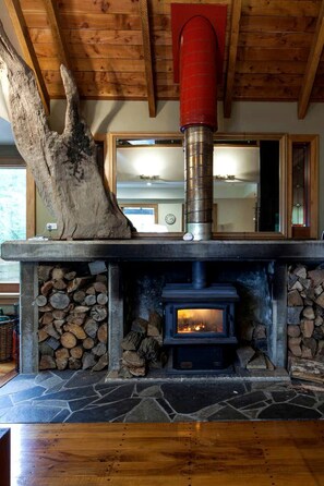 Una chimenea de piedra con estufa de leña, un gran tronco de árbol y una chimada roja.