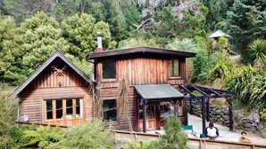A wooden cabin with a porch and a chimney, surrounded by dense forest.