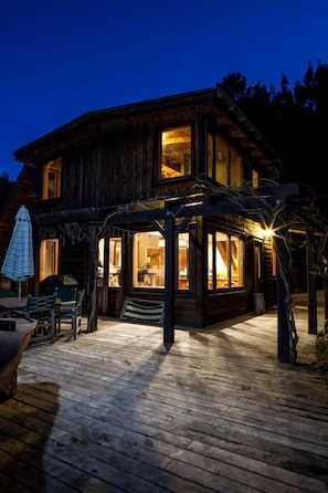 A wooden cabin with a deck, large windows, and a covered patio area.