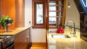 A kitchen with wooden beams, a granite countertop, a red kettle, and a window.