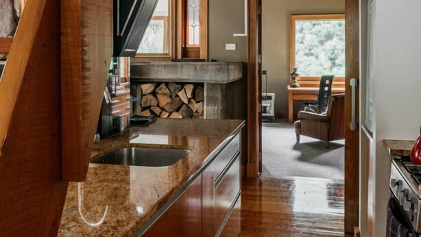A kitchen with wooden beams, a granite countertop, and a stone fireplace.