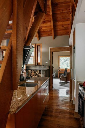 A kitchen with wooden beams, a granite countertop, and a stone fireplace.