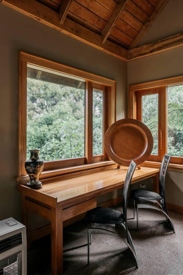 A wooden dining table with chairs, a vase, and a plate, with large windows offering a view of greenery. - Unique Off-Grid Little River Accommodation Ideal for a South Island Getaway on the Banks Peninsula (Little River)