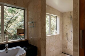 Ein Badezimmer mit einer Badewanne, einer Dusche und einem Fenster mit Blick auf Bäume.