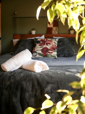 Ein Bett mit gerolltem Handtuch, einem blumigen Kopfkissen und einer dunklen Decke.