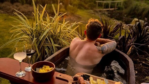 A person relaxing in a hot tub with a wooden tray of food and drinks.