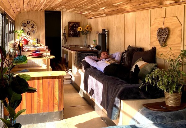 Un intérieur chaleureux en bois, avec un lit, une table sur laquelle se trouve une bouilloire et une horloge murale.