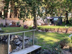 A garden with a pond, a wooden bridge, and a vehicle in the background.