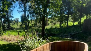 A wooden hot tub with a curved design, surrounded by greenery and trees.