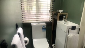 A compact bathroom with a toilet, a sink, and a window with blinds.