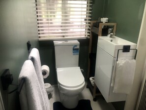 Een kleine badkamer met toilet, wastafel en raam met zonwering.